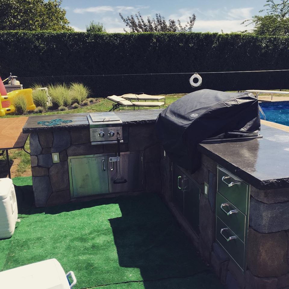 Outdoor kitchen with stone grill next to pool